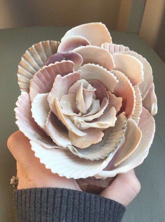 a person's hand holding a flower made out of seashells