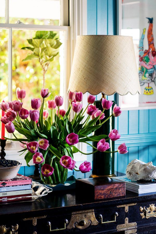 pink tulips are in a vase on a table next to a lamp and books