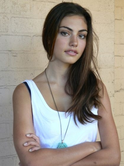 a woman standing with her arms crossed in front of a brick wall and wearing a white tank top