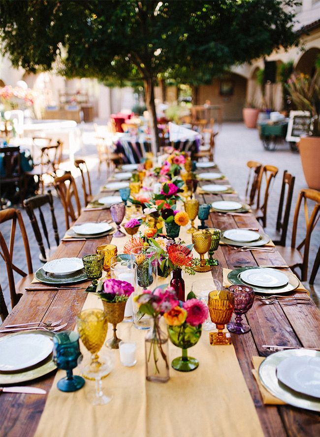 a long table with plates and vases on it is set for an outdoor dinner