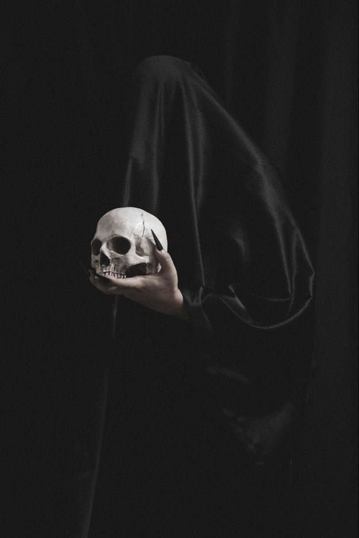 a person holding a human skull in their left hand and wearing a black hoodie