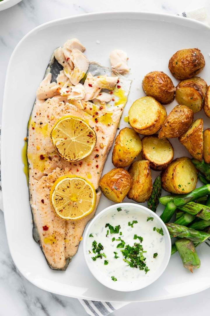 a white plate topped with fish, potatoes and asparagus