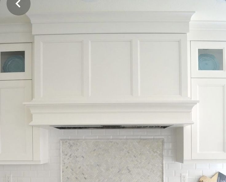 a kitchen with white cabinets and marble counter tops, an oven hood over the stove