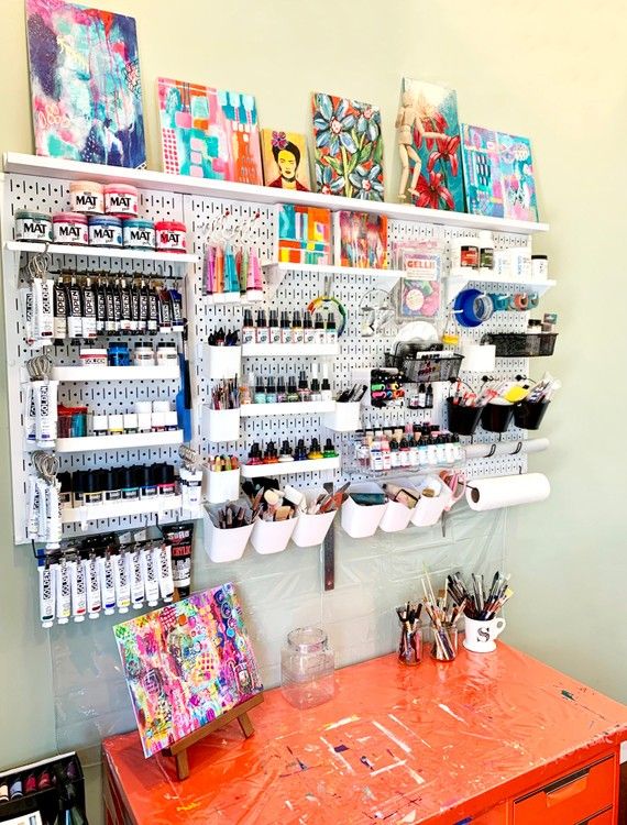 an orange desk with lots of art supplies on the wall and shelves above it that are filled with various items