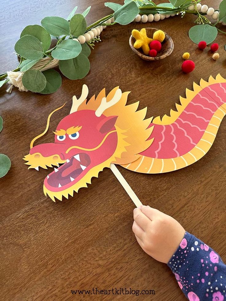 a child is holding a paper dragon on a wooden table with green leaves around it