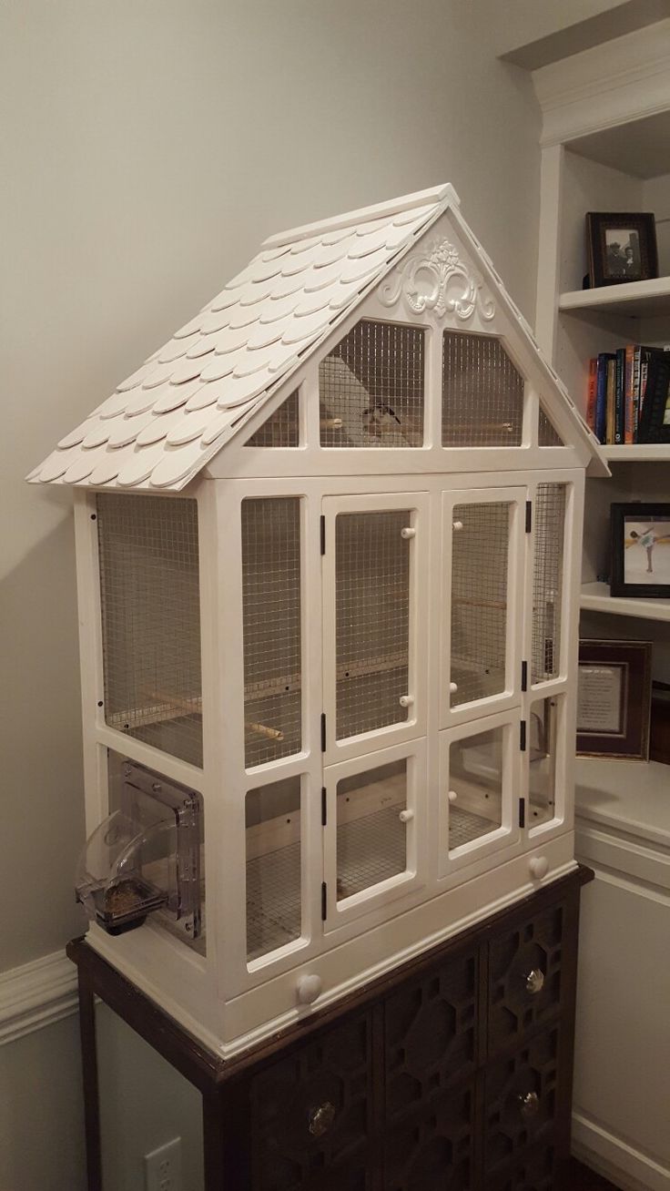 a large white bird cage sitting on top of a wooden dresser next to a book shelf