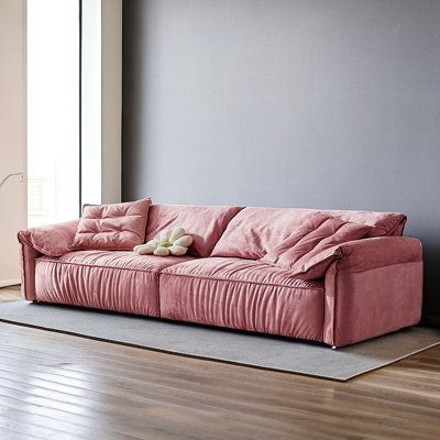 a pink couch sitting on top of a hard wood floor next to a gray wall