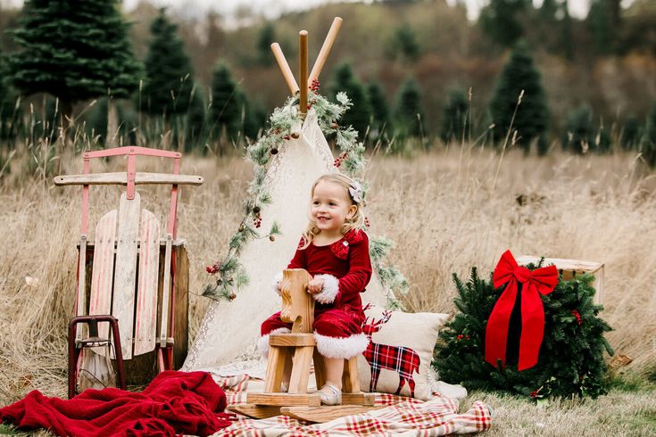 a baby sitting on a wooden chair in front of a teepee with christmas decorations