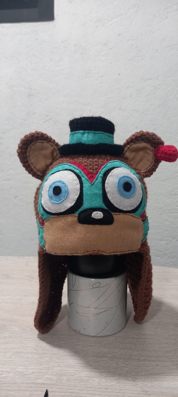 a stuffed animal hat with big eyes on top of a cup