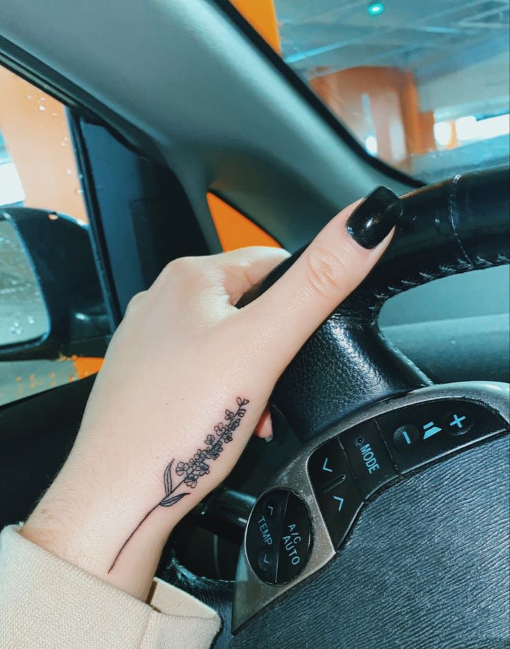 a woman's hand on the steering wheel of a car with a small tattoo