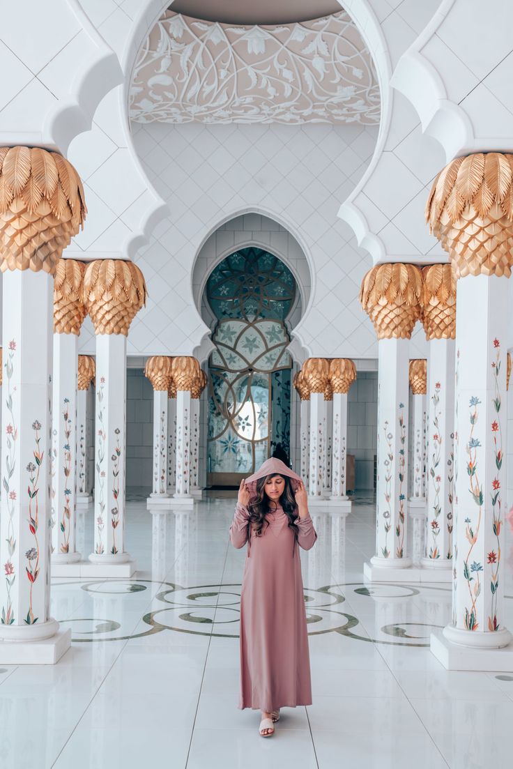 a woman in a pink dress is standing in an ornate room with columns and arches