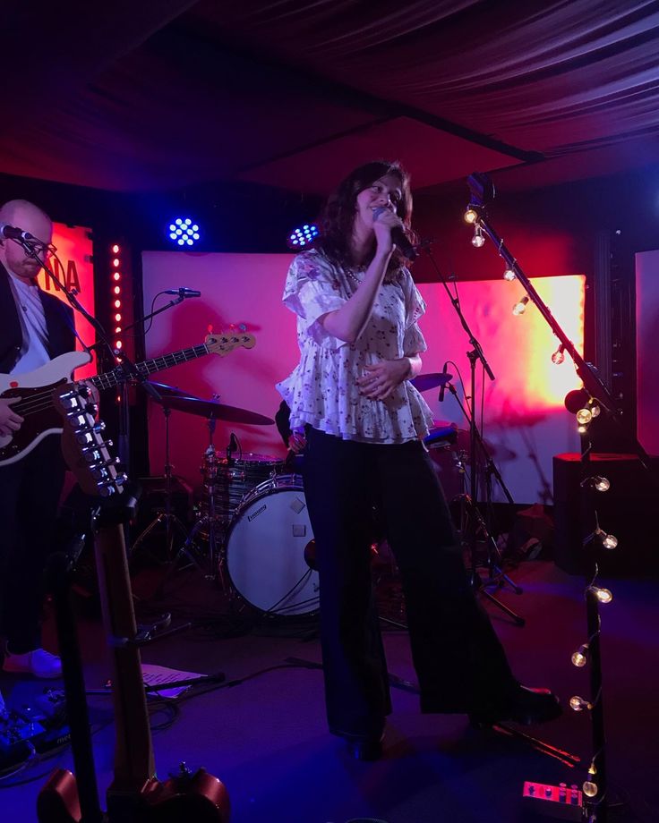 a woman singing into a microphone while standing in front of two other people on stage