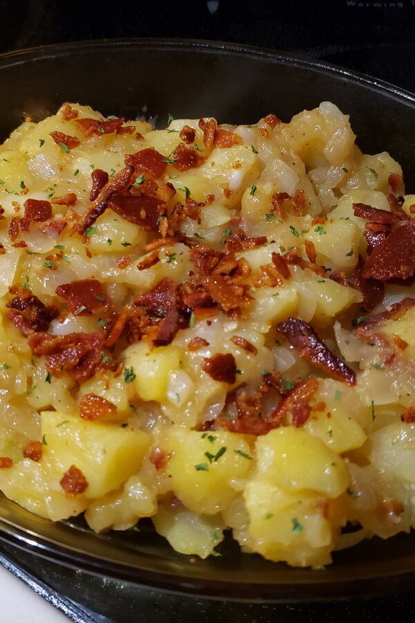 a black plate topped with potatoes covered in bacon and cheese on top of a stove