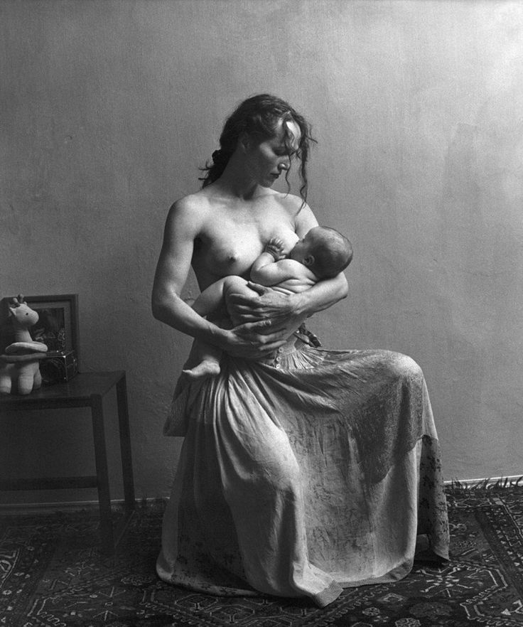 a black and white photo of a man with no shirt holding a baby in his lap