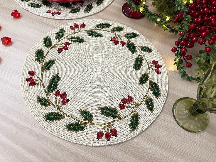 two placemats with holly designs on them sitting on a table next to christmas decorations