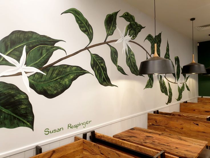 the interior of a restaurant with wooden tables and green leaves painted on the wall behind them