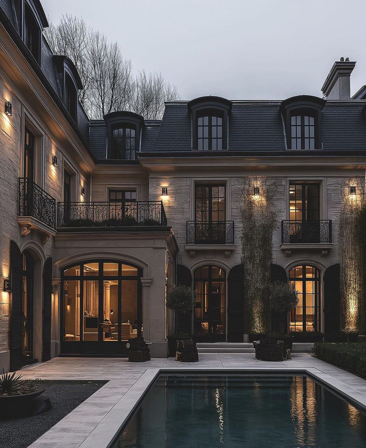 a large house with a swimming pool in front of it at night, lit up by lights