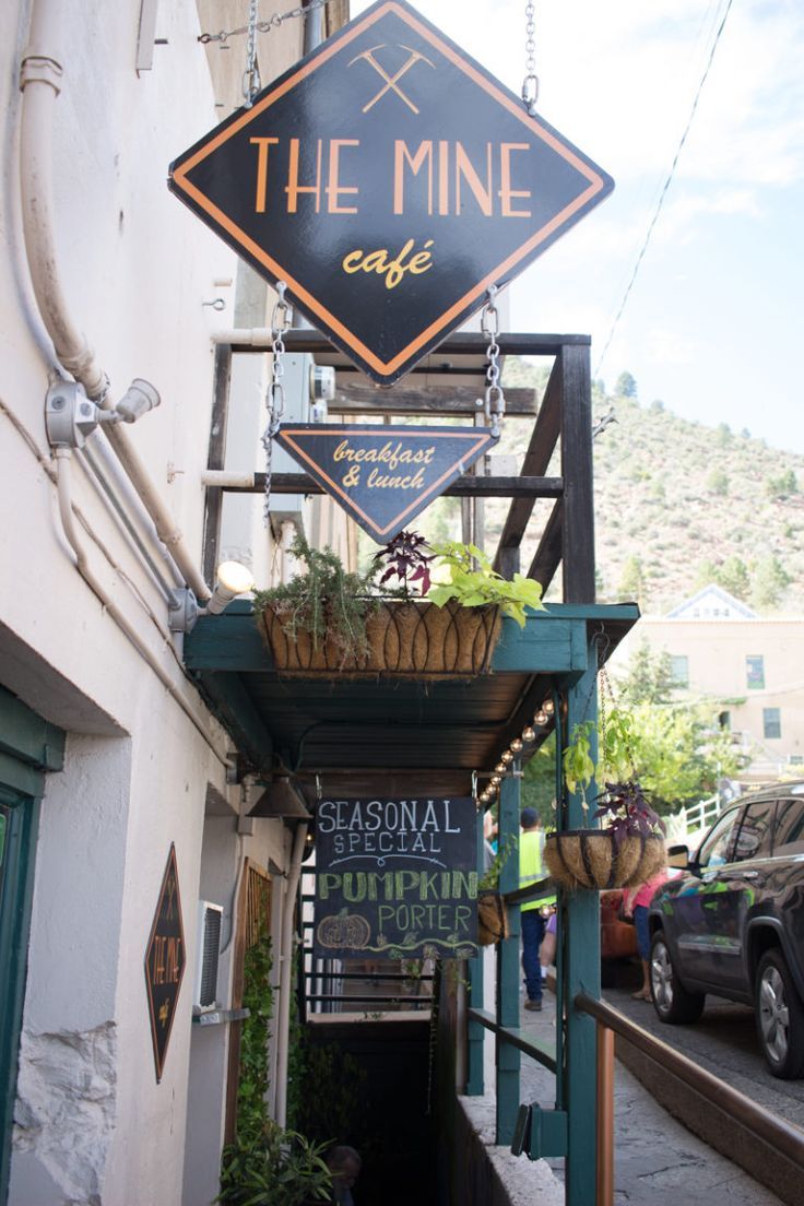 the sign for the mine cafe is hanging from the side of the building with potted plants on it