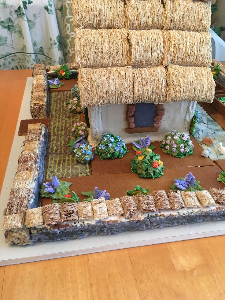 a cake made to look like a house with thatched roof and flowers on the ground