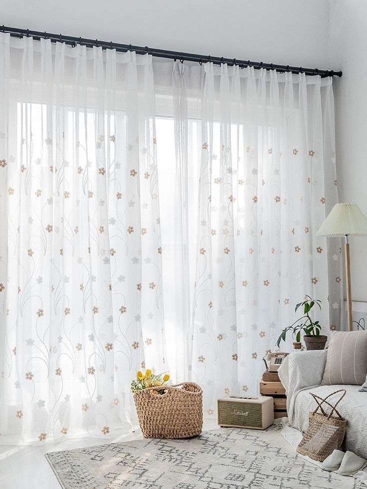 a white living room with sheer curtains and flowers on the window sill in front of it