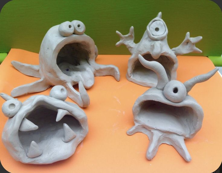 three white clay sculptures sitting on top of an orange table next to each other with eyes and mouths