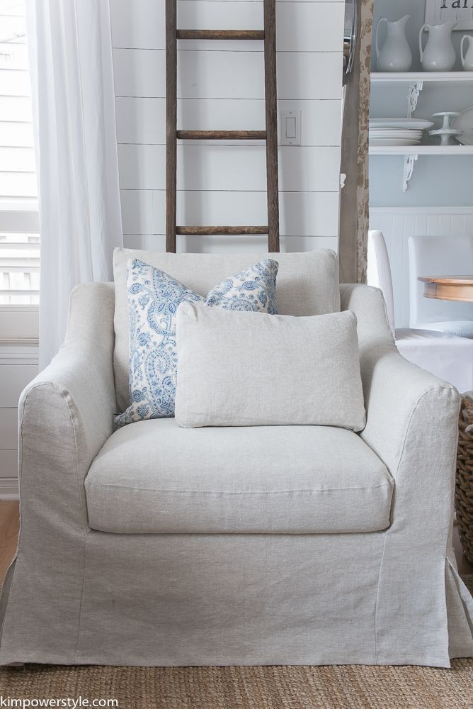 a white couch with blue and white pillows in front of a wooden leaning ladder that is next to a window