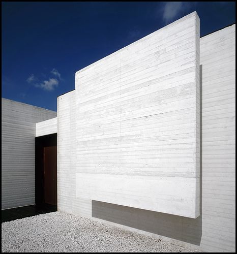 a white building with two doors in front of it and gravel on the ground next to it