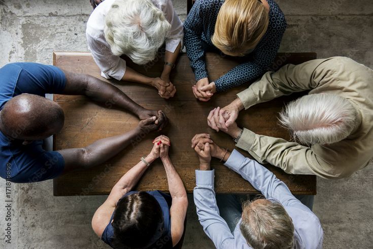 four people sitting at a table with their hands together