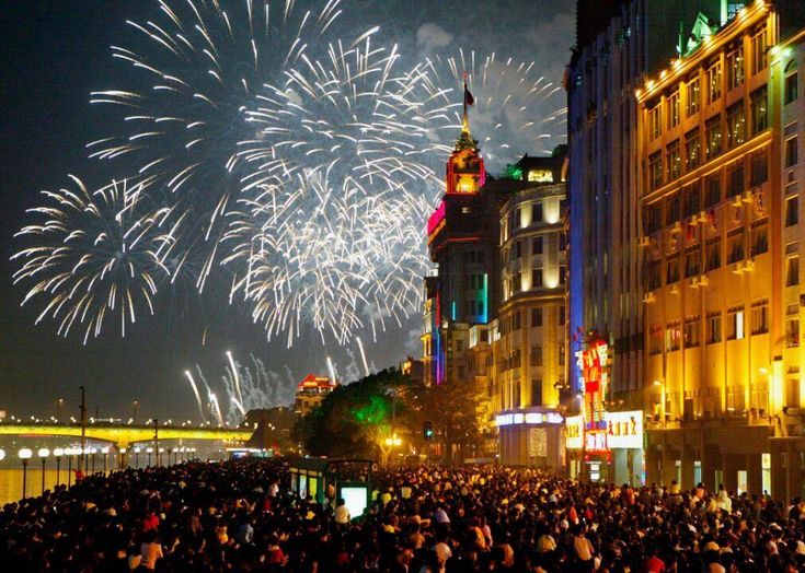 fireworks are lit up in the night sky over a city street with buildings and people