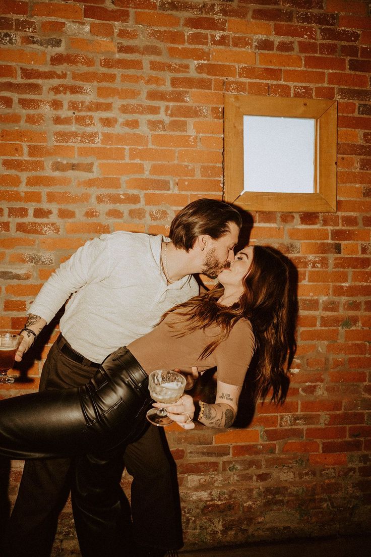 a man and woman kissing in front of a brick wall