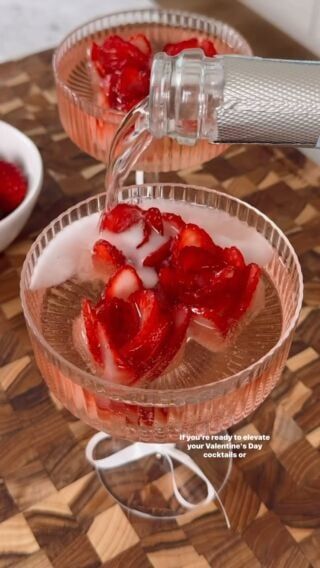 two glasses filled with ice and strawberries on top of a wooden table next to bowls of strawberries