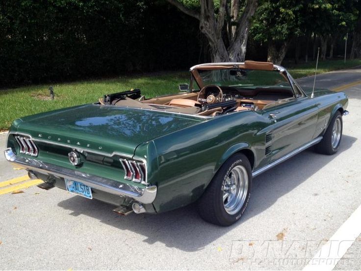 an old green mustang convertible parked on the side of the road