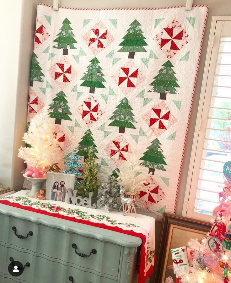 a quilted christmas tree wall hanging next to a dresser and table with ornaments on it