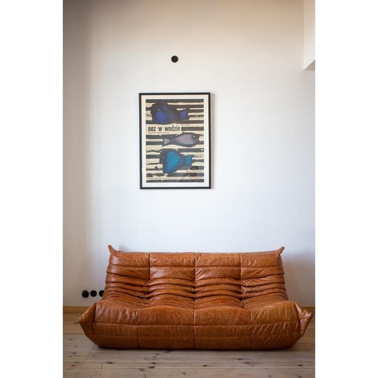 a brown leather futon is in front of a white wall with a framed poster on it