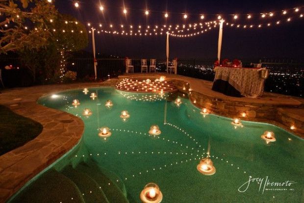 an outdoor pool with candles and lights around it at night, surrounded by greenery