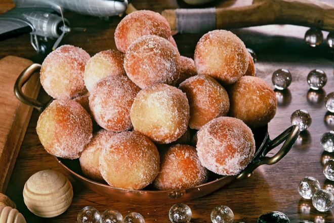 a bowl filled with sugar covered donuts on top of a wooden table next to other items