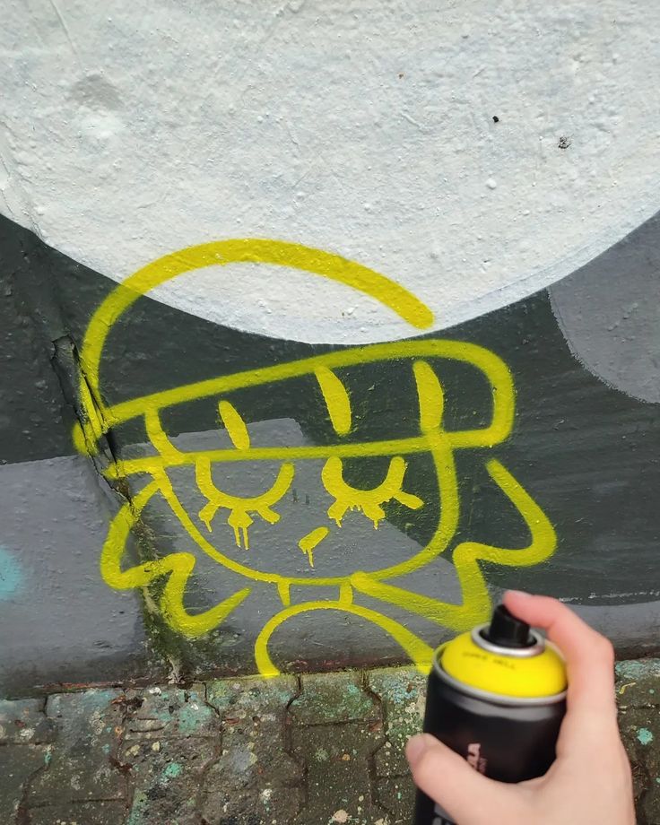 someone spray painting graffiti on the side of a wall with yellow and black paint,