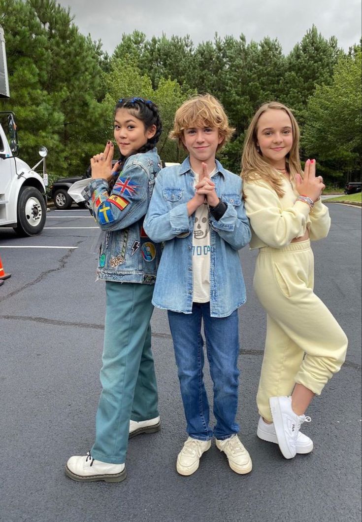 three young people standing in the middle of a parking lot with one holding up his peace sign