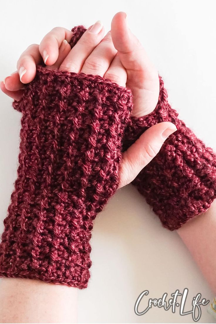 a woman's hand is holding up a crocheted arm warmer in red