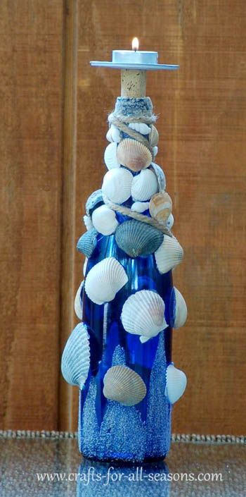 a blue glass candle holder with seashells on it and a lit candle in the middle