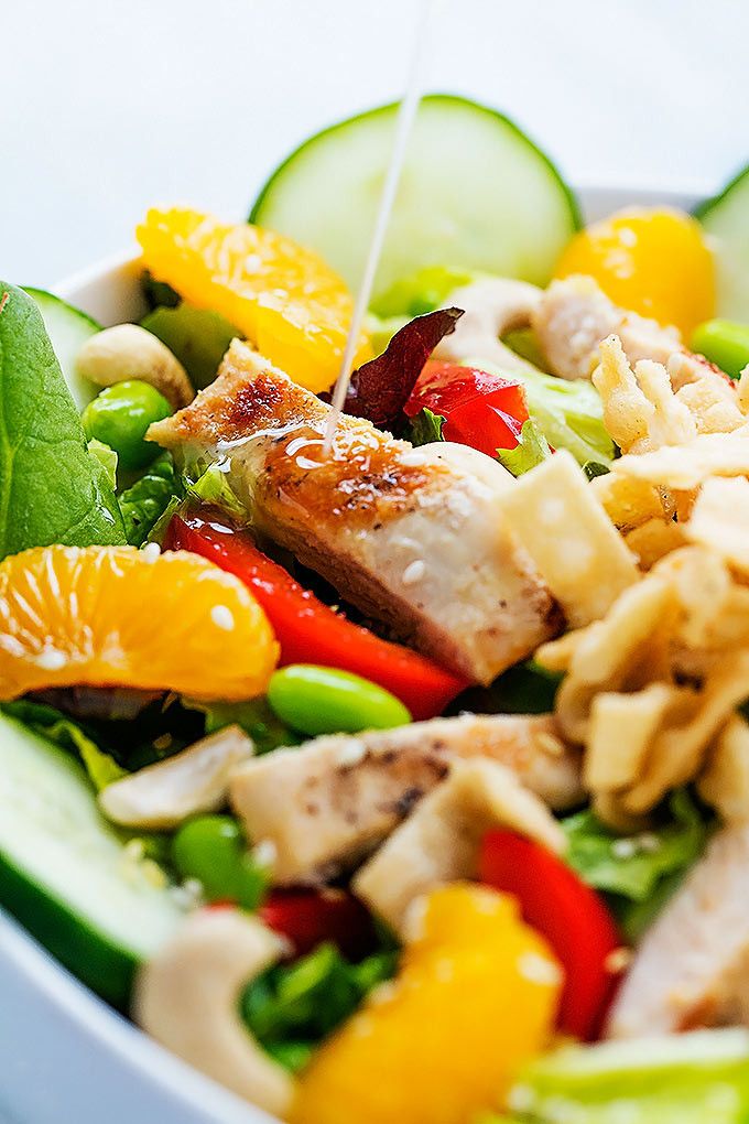 a salad with chicken, oranges, cucumbers and other vegetables is being drizzled with dressing