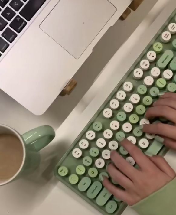 a person typing on a green keyboard next to a cup of coffee