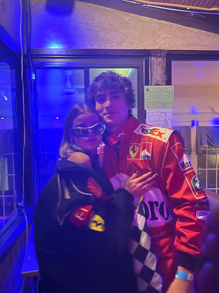 a man and woman standing next to each other in front of a blue light wearing racing gear