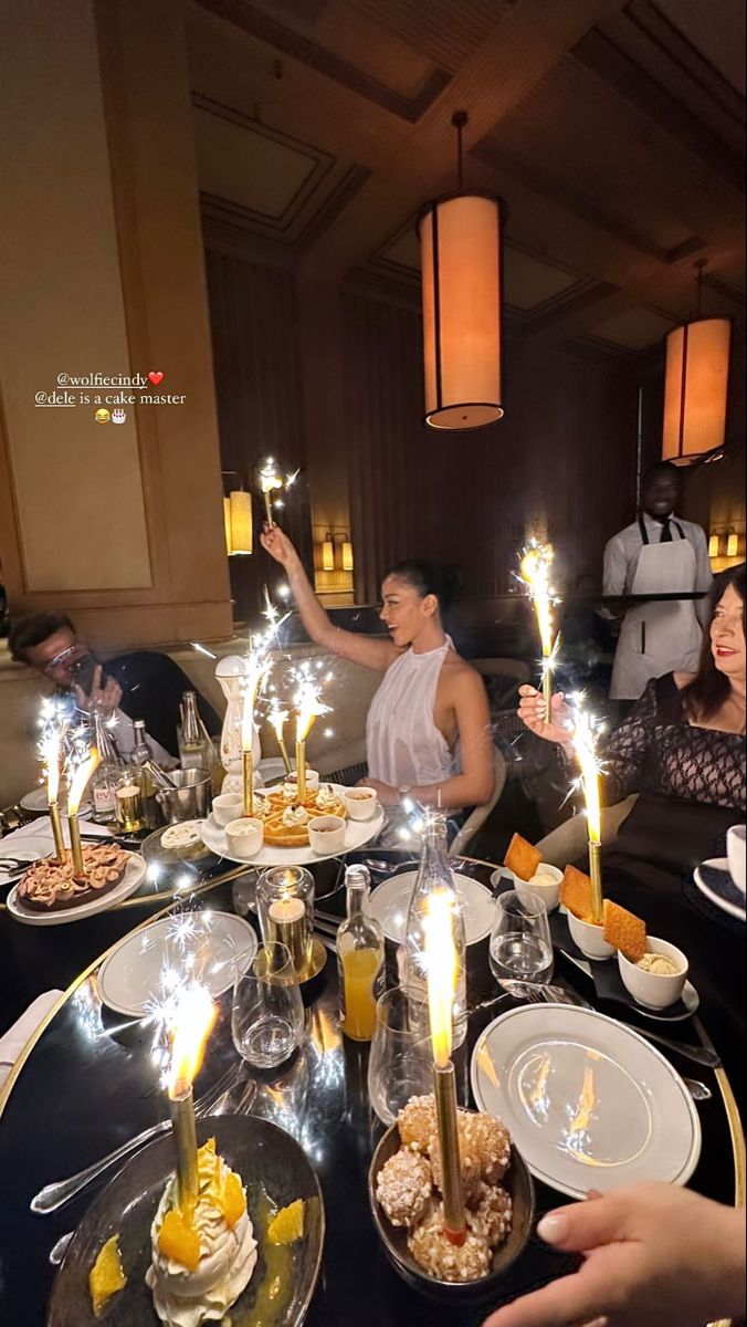 people are sitting at a table with candles in the air and food on plates around them