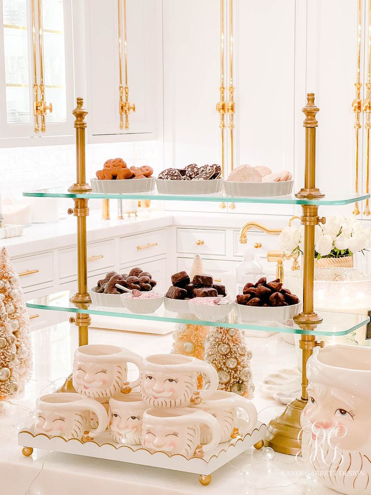 an assortment of pastries on glass shelves in a white and gold themed kitchen area