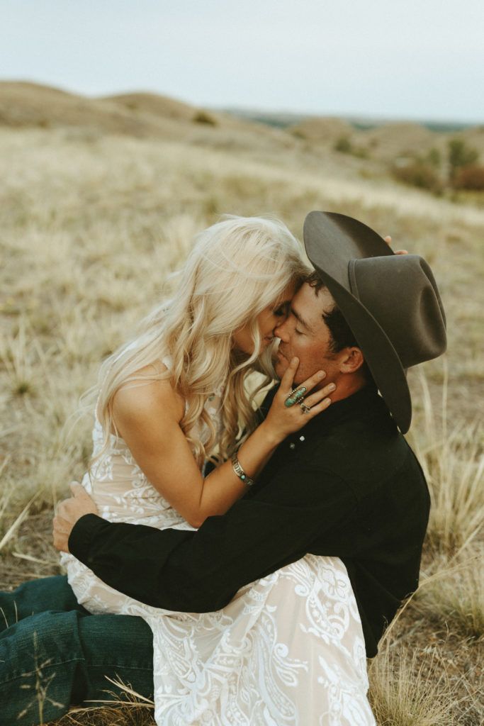 a man in a cowboy hat hugging a woman on the side of a hill with dry grass