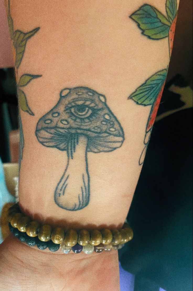 a woman's arm with a mushroom tattoo on it and beads around the wrist