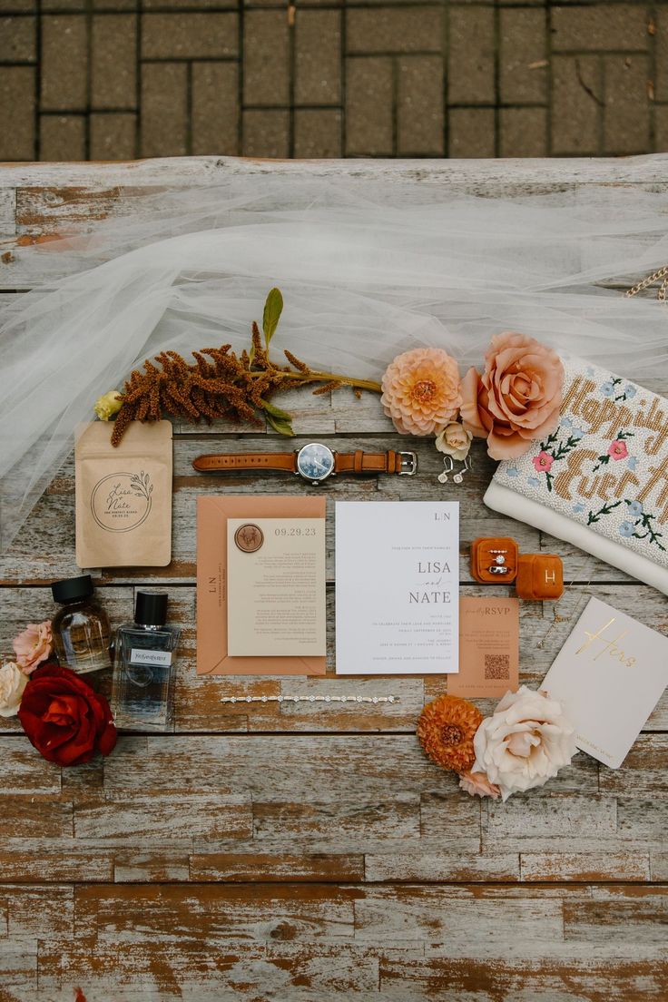 the wedding stationery is laid out on top of an old wooden table with flowers