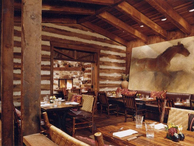 a restaurant with wooden tables and chairs, paintings on the wall behind them in an old log cabin