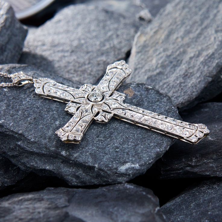 This breathtaking platinum cross shaped pendant features a pierced design with milgrain details and is centered with a round old European cut diamond, weighing 0.28 carats, in a full bezel setting. The center is accented with a total of eighty-eight (88) bead set round cut diamonds. The pendant is topped by a matching bail, bead set with three (3) round single cut diamonds. The pendant measures 71.5mm long, by 46.7mm wide and 4.7mm thick on an 18-inch long, fourteen karat white gold cable link chain, finished with a lobster clasp. Luxury Cross-shaped Diamond Cut Necklace, Luxury White Gold Cross Necklace With Diamond Accents, Classic Diamond Accents Cross Pendant Necklace, Classic Diamond White Cross Necklace, Milgrain Diamond Jewelry In White Gold, White Gold Diamond Jewelry With Milgrain Detail, Classic Diamond White Crucifix Cross Necklace, Diamond White Cross Necklace With Single Cut Diamonds, Classic Cross Necklace With Diamond Accents